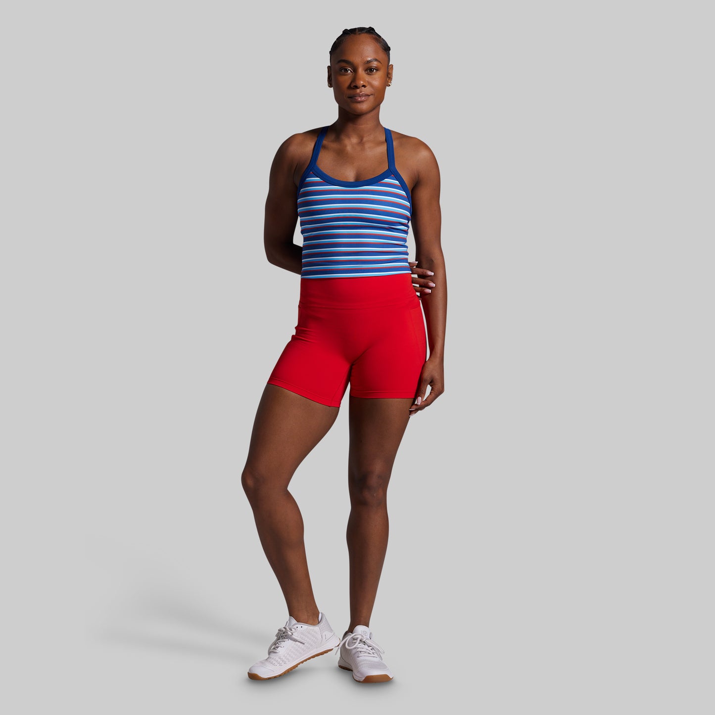 Woman wearing a blue striped sports bra and red shorts on a gray background
