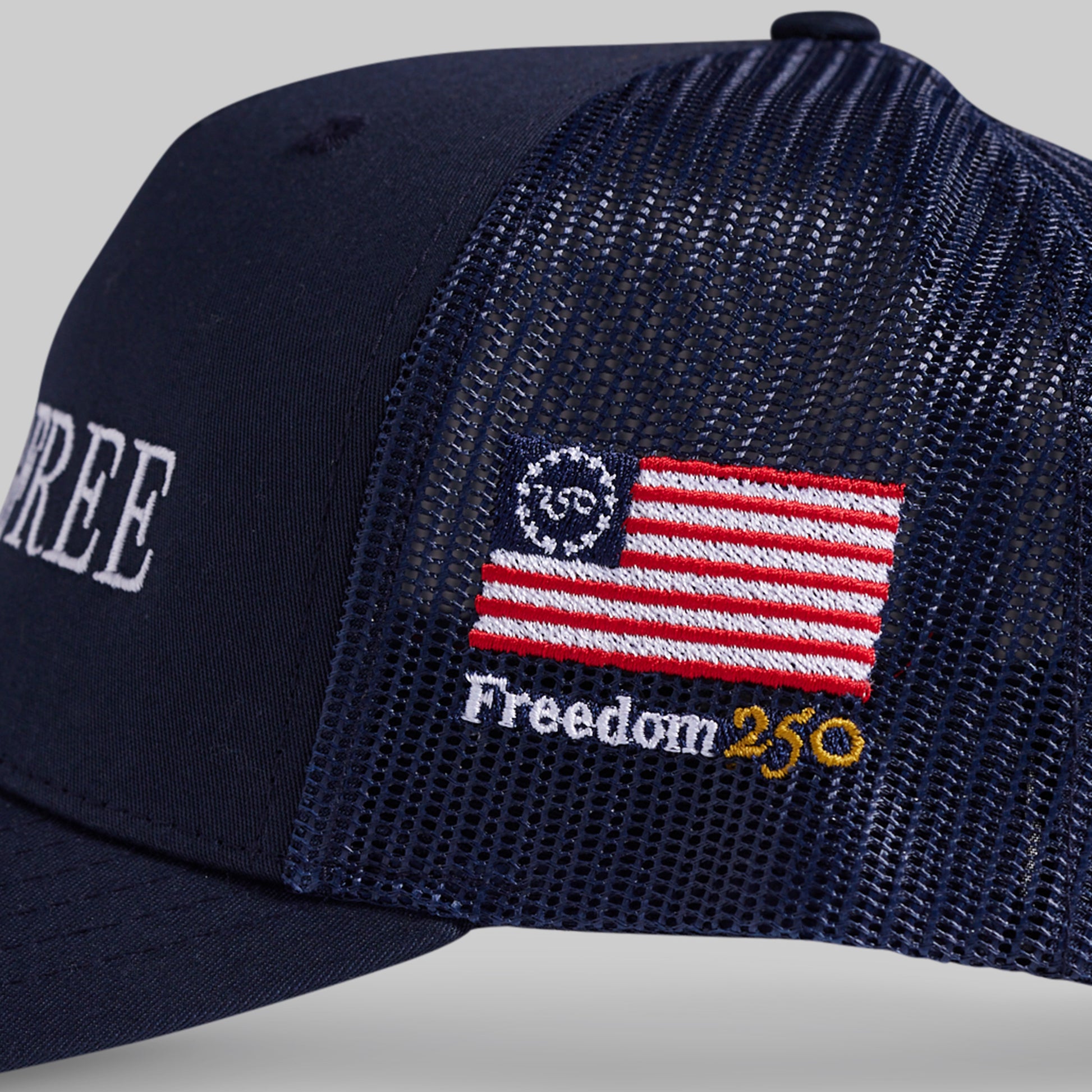 Navy blue cap with American flag patch and 'Freedom 250' text on a gray background