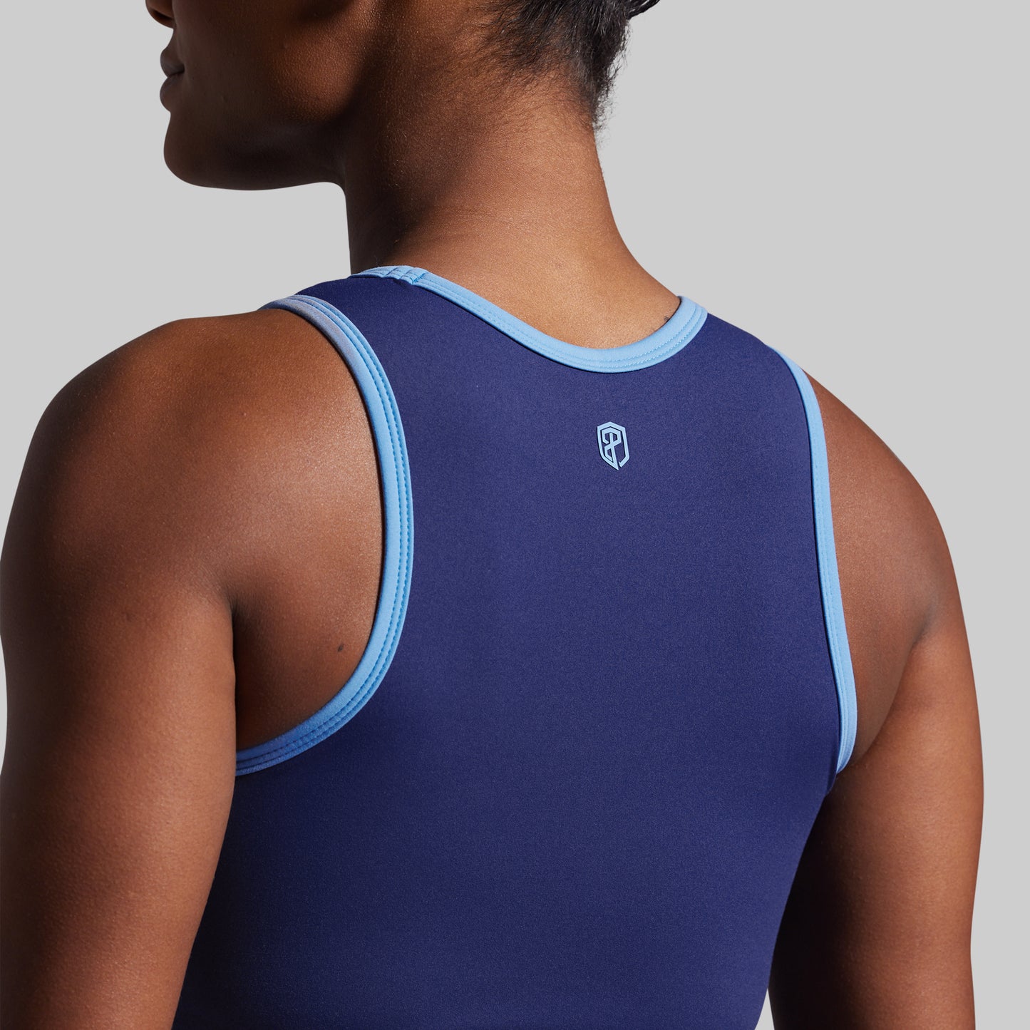 Person wearing a blue tank top with light blue trim on a gray background
