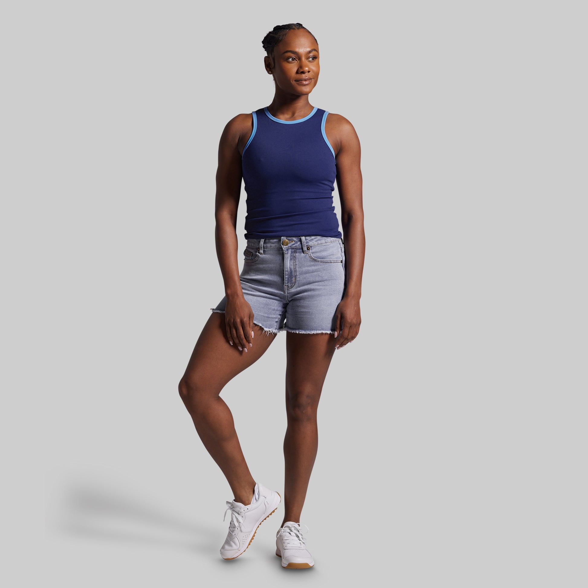 Woman wearing a blue tank top and denim shorts on a gray background