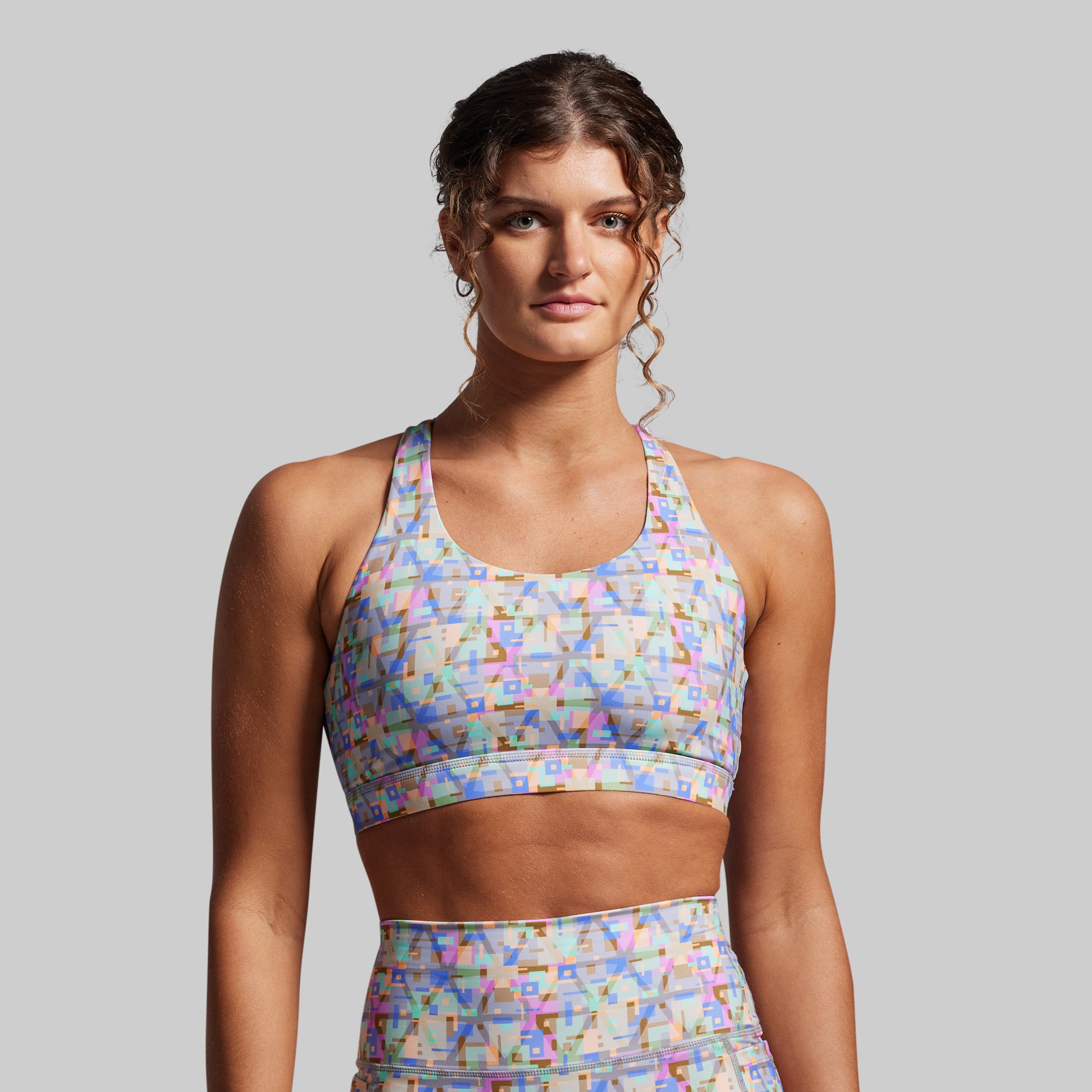 Woman wearing a colorful patterned sports bra and leggings on a gray background