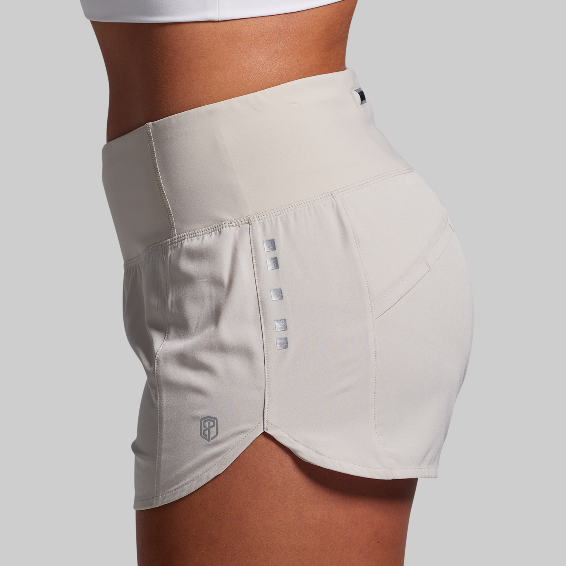 Beige athletic shorts with a brand logo on a light gray background