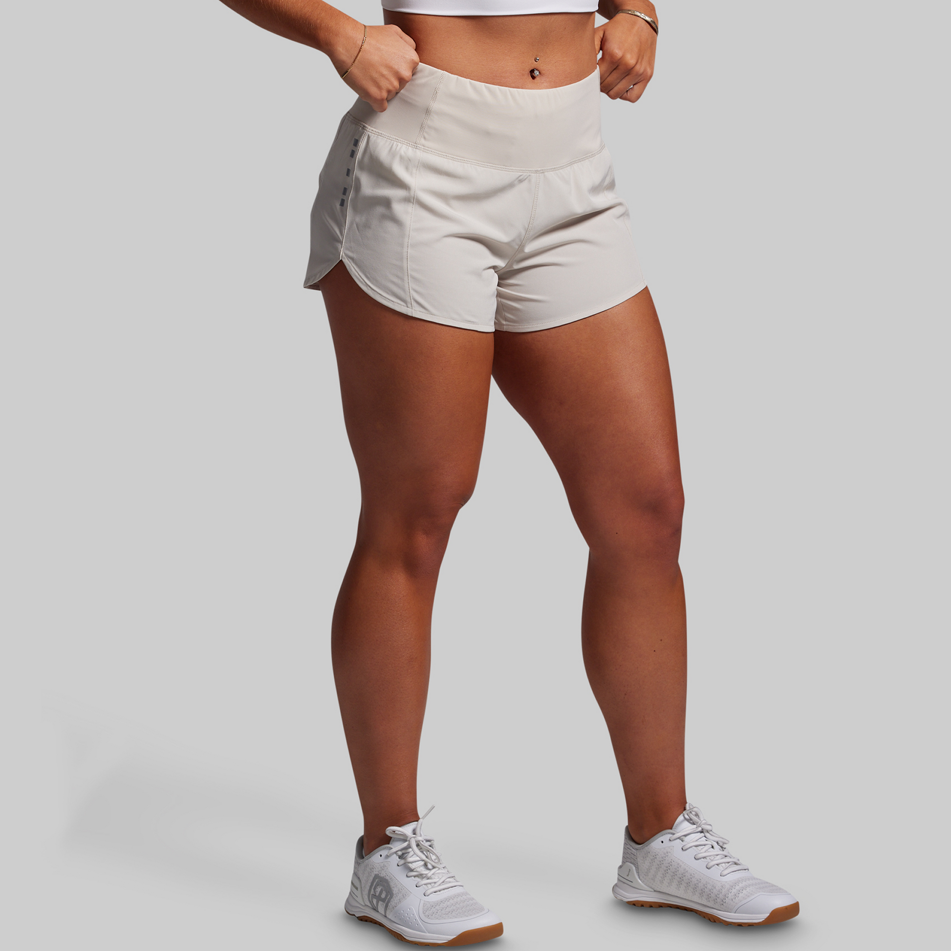 Person wearing light-colored shorts and white sneakers on a plain background