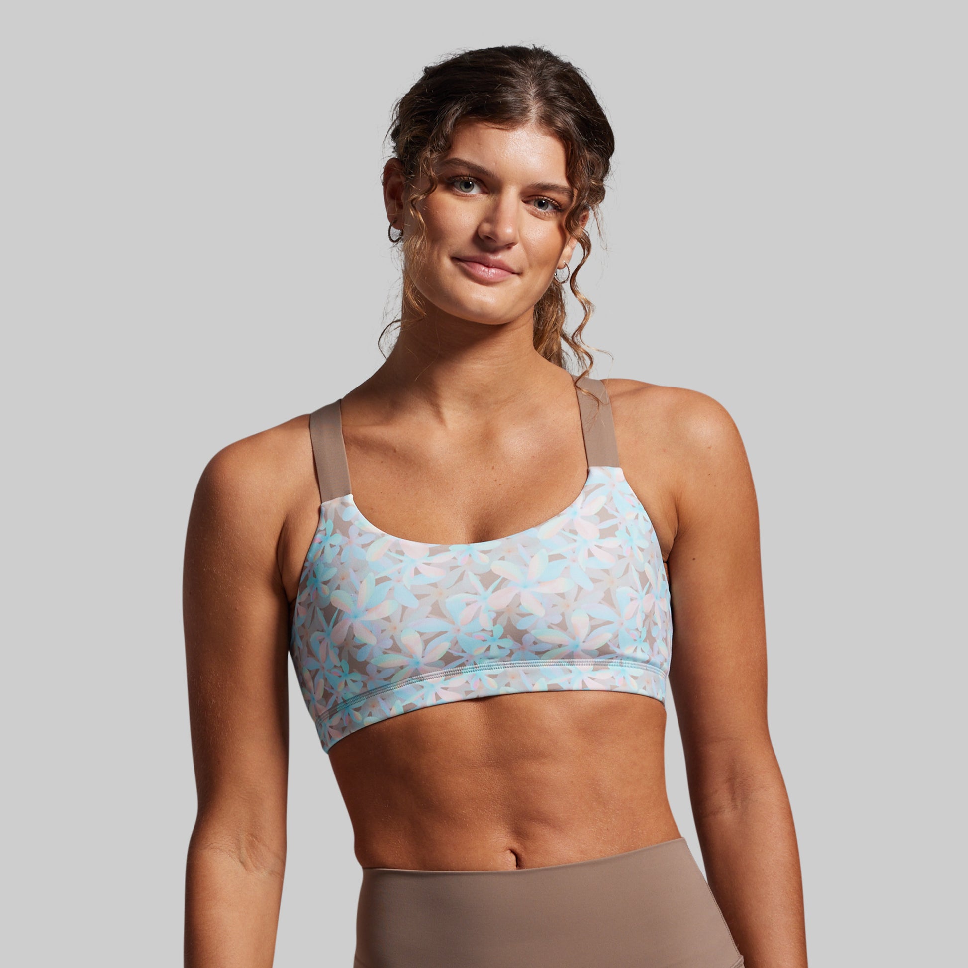 Woman wearing a light blue sports bra with floral pattern on a gray background