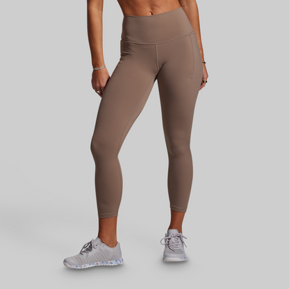 Person wearing beige leggings and white sneakers on a gray background