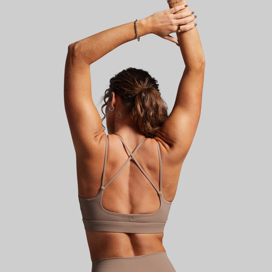 Woman wearing a beige sports bra and leggings with a plain background