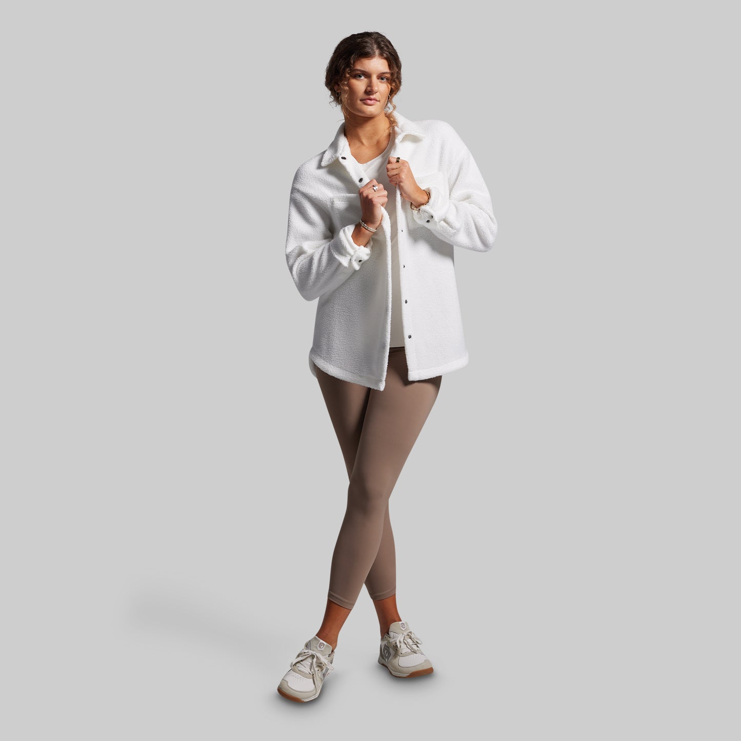 Woman wearing a white shirt and brown leggings on a gray background