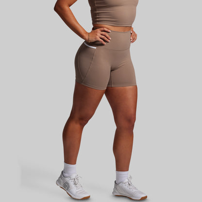 Person wearing brown athletic shorts and a matching sports bra on a gray background