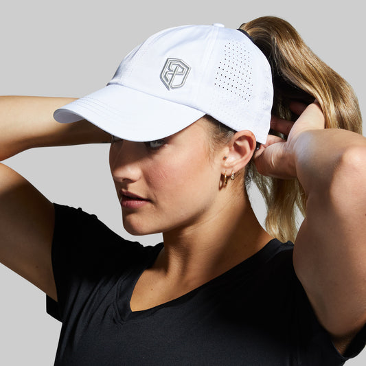 Woman adjusting a white cap with a logo on a gray background